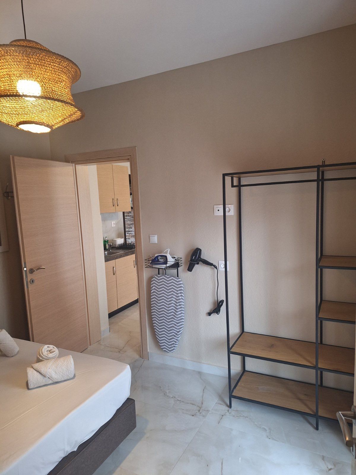 Bedroom with open door, ironing board, metal clothing rack, and a bed in a neutral-toned room