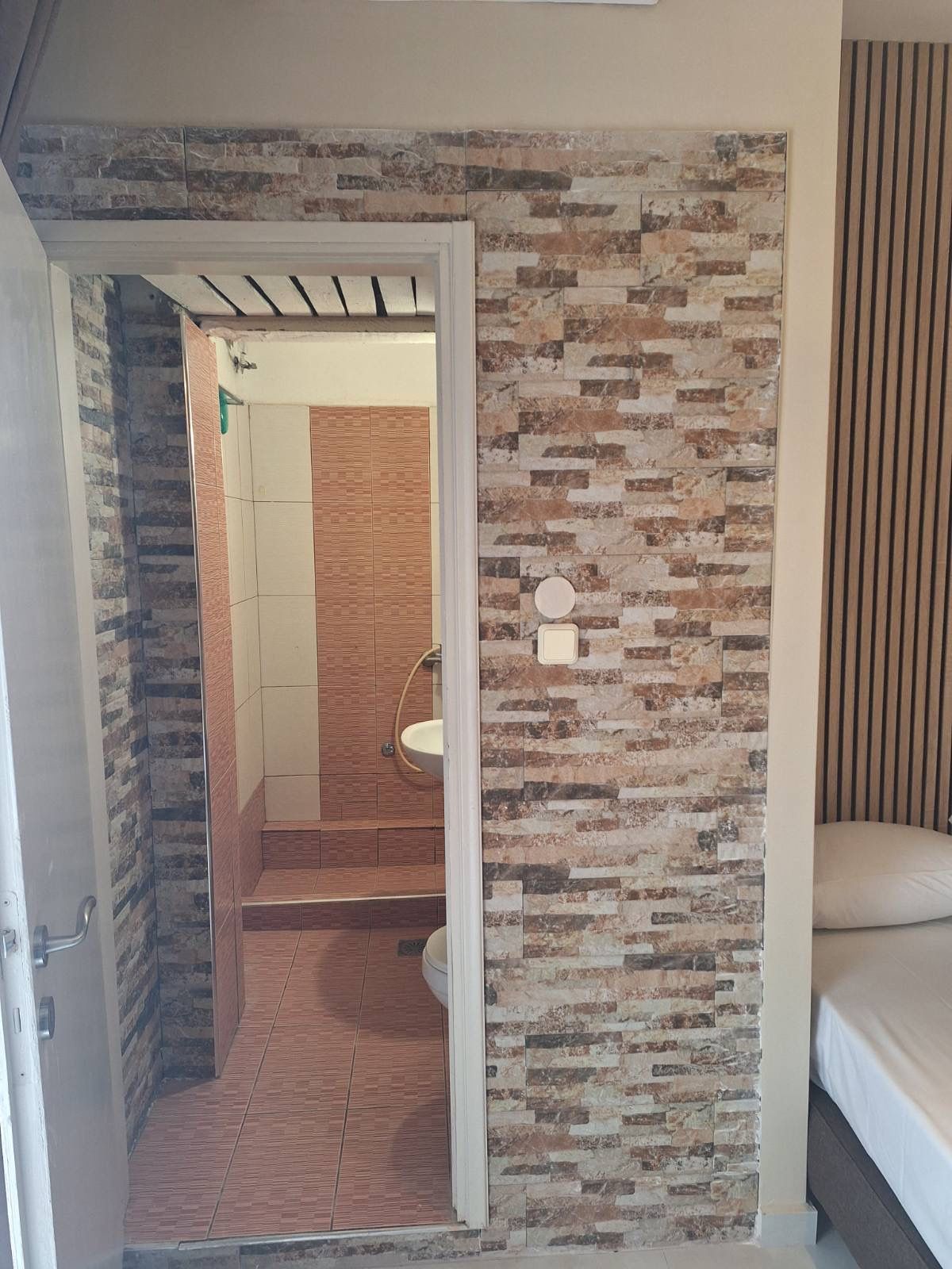 Small room with brick-pattern wall and open doorway to a bathroom; bed edge visible on the right.