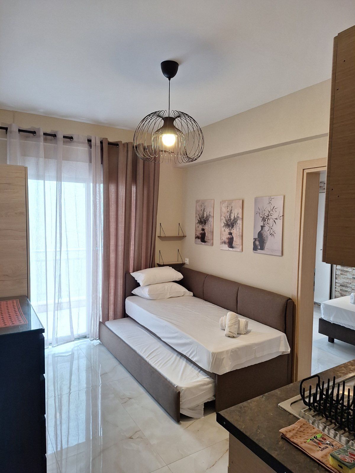 Small bedroom with a single bed, soft pink curtains, pendant light, and wall art.