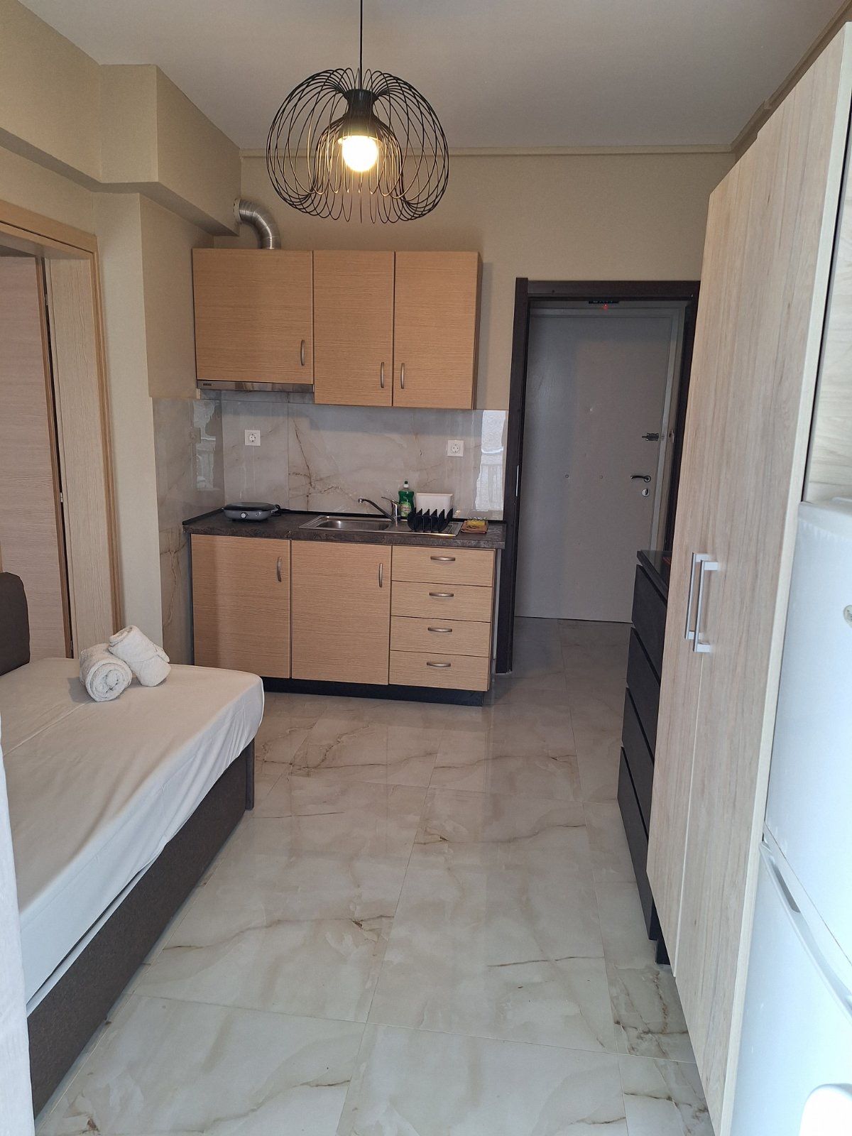 Small furnished studio room with bed, kitchenette, wardrobe, and marble floor