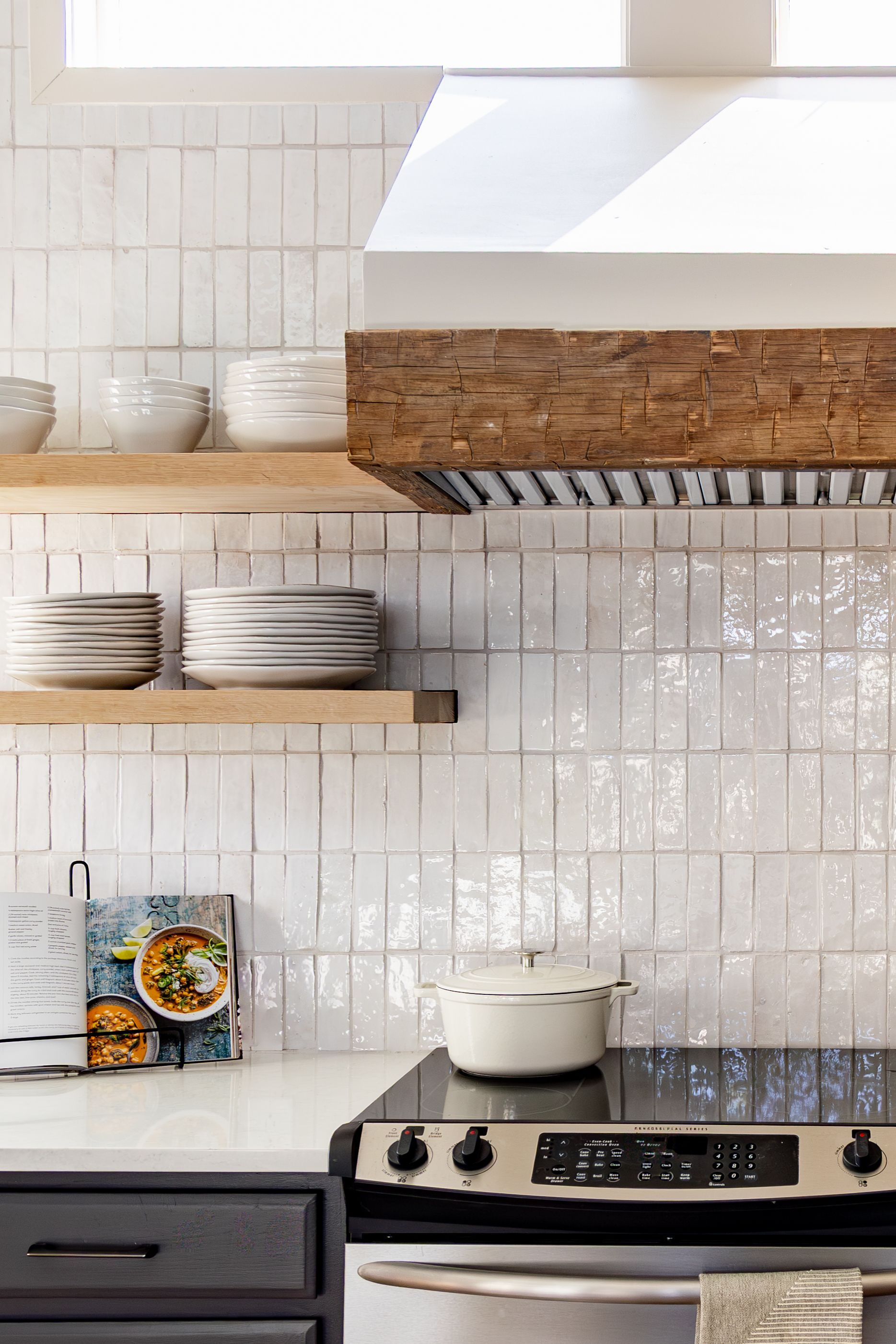 Kitchen with white tiled backsplash, wooden range hood, open shelves, and stovetop.
