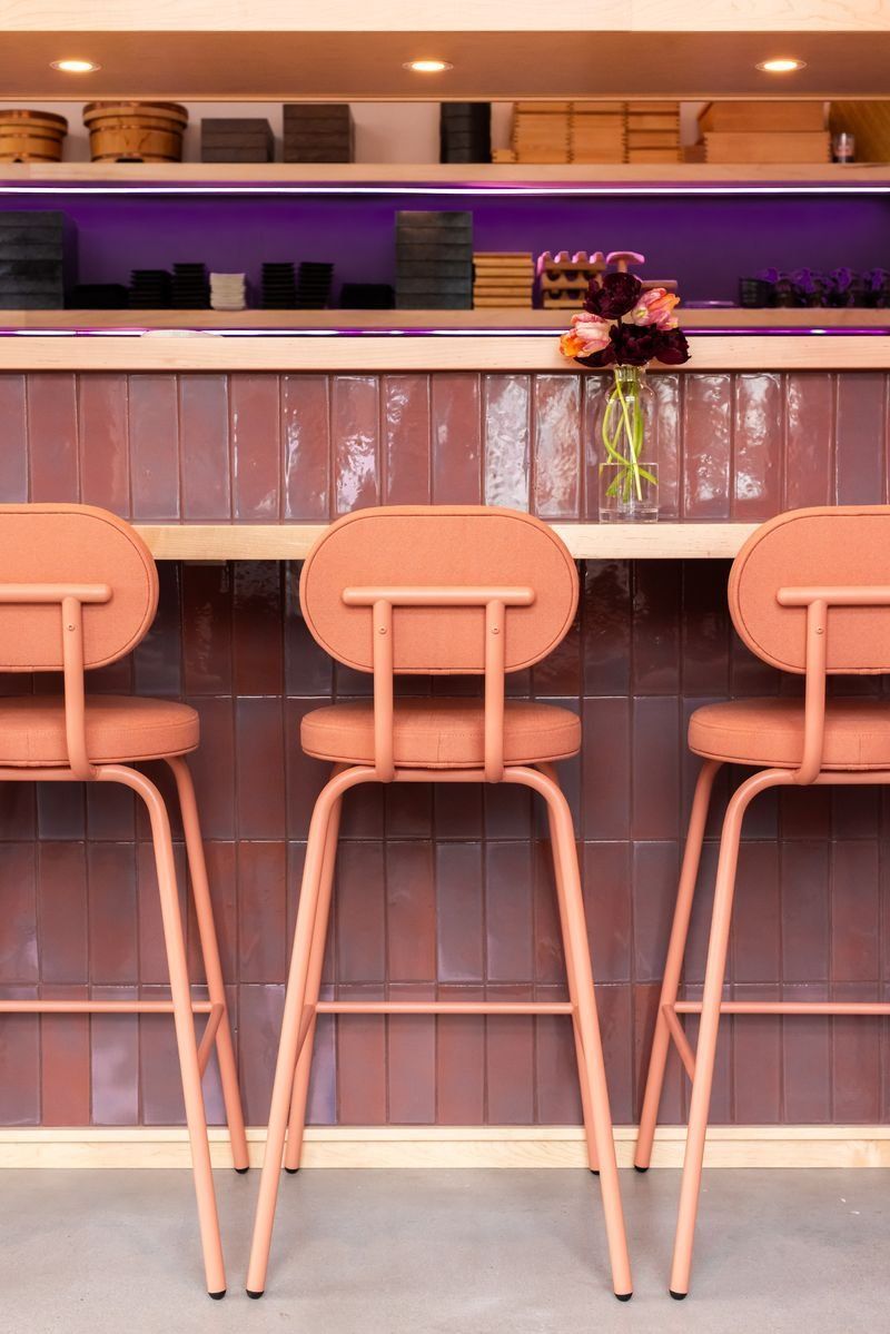 A row of pink bar stools sitting next to a wooden counter in a restaurant.