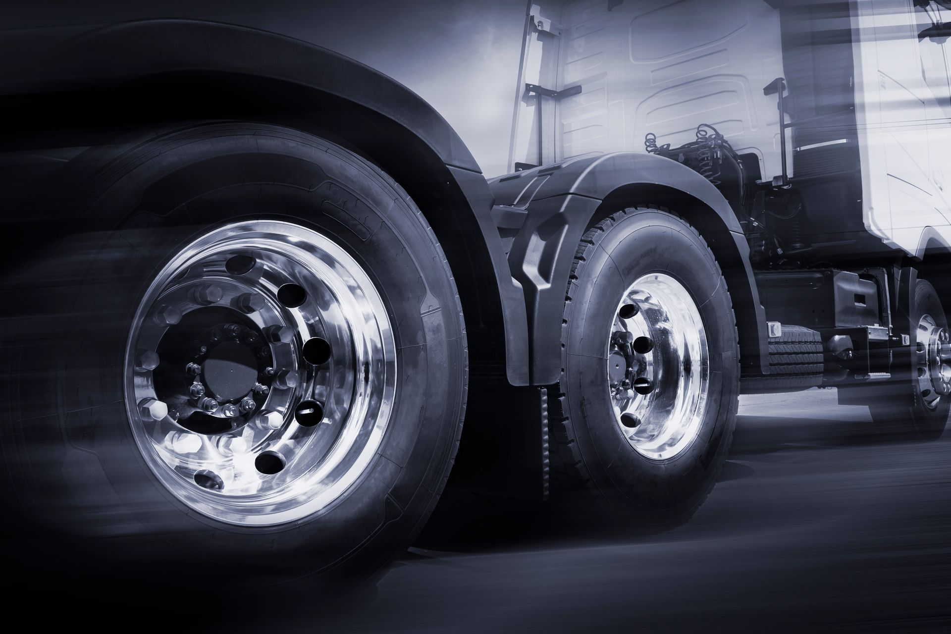 Close-up of a semi truck’s chrome wheels and tires on a highway, with motion blur in the background