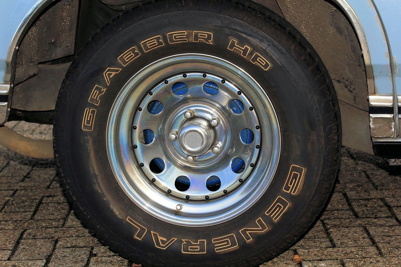 Close-up of a car wheel with a silver rim and black tire on a cobblestone surface.
