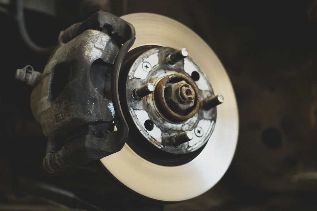 Close-up of a car brake rotor and caliper with a worn wheel hub in a garage.