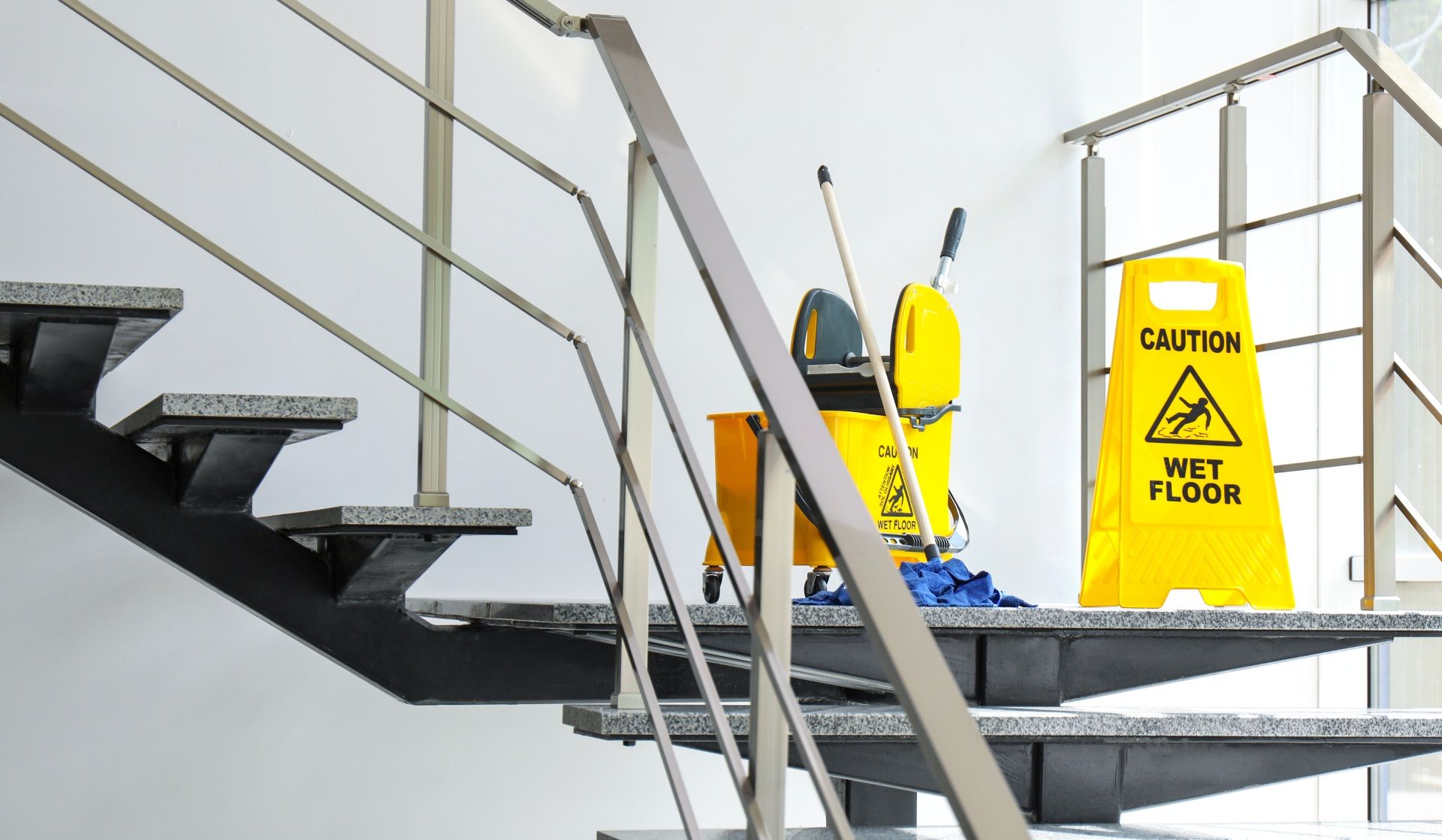 A yellow wet floor sign is on the stairs next to a mop and bucket