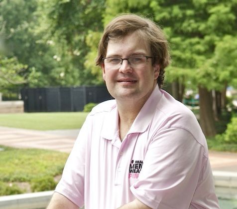 A man in a suit and glasses is standing in front of a kind lending sign.