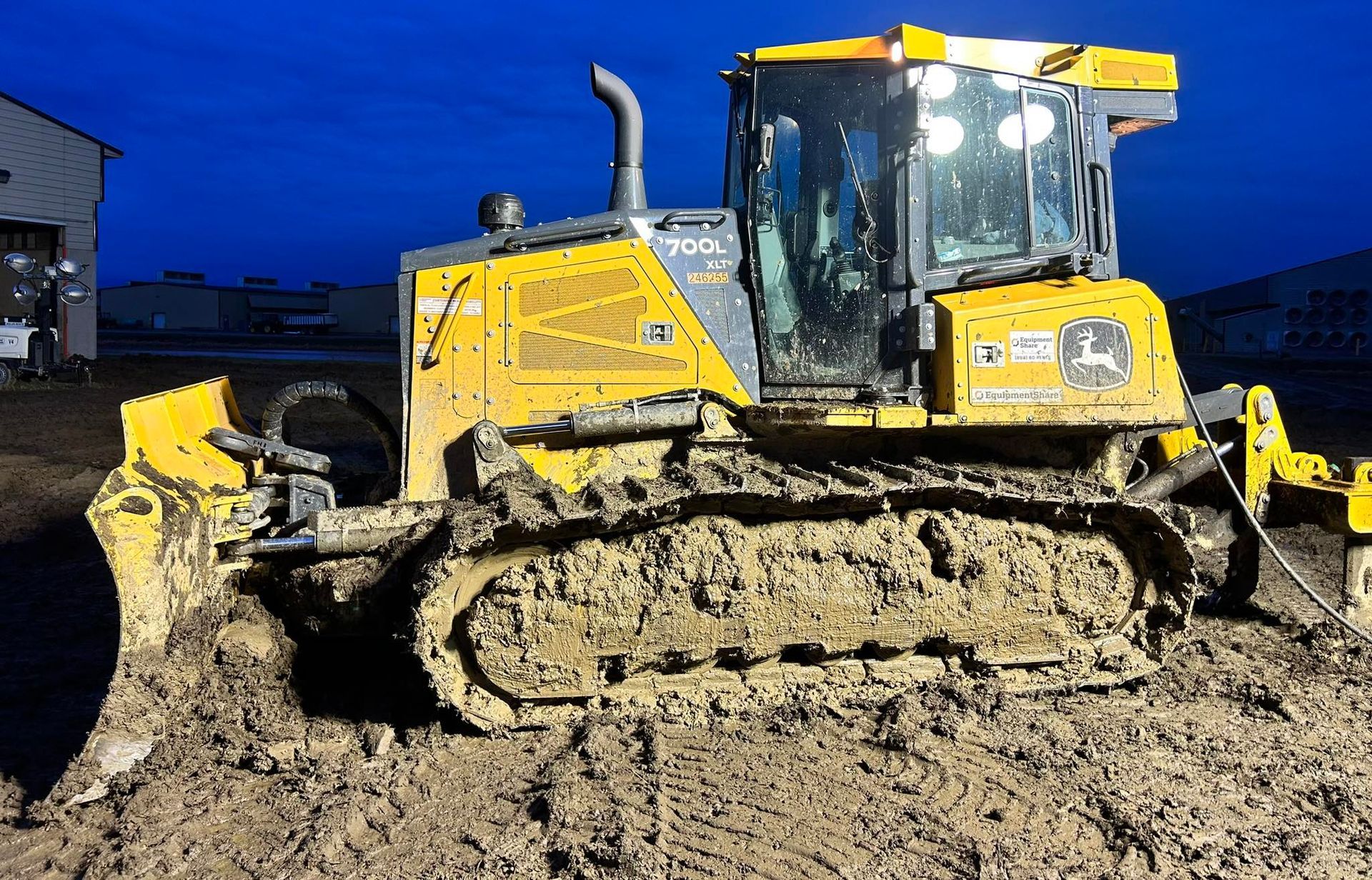Yellow John Deere bulldozer covered in mud, parked on muddy ground.