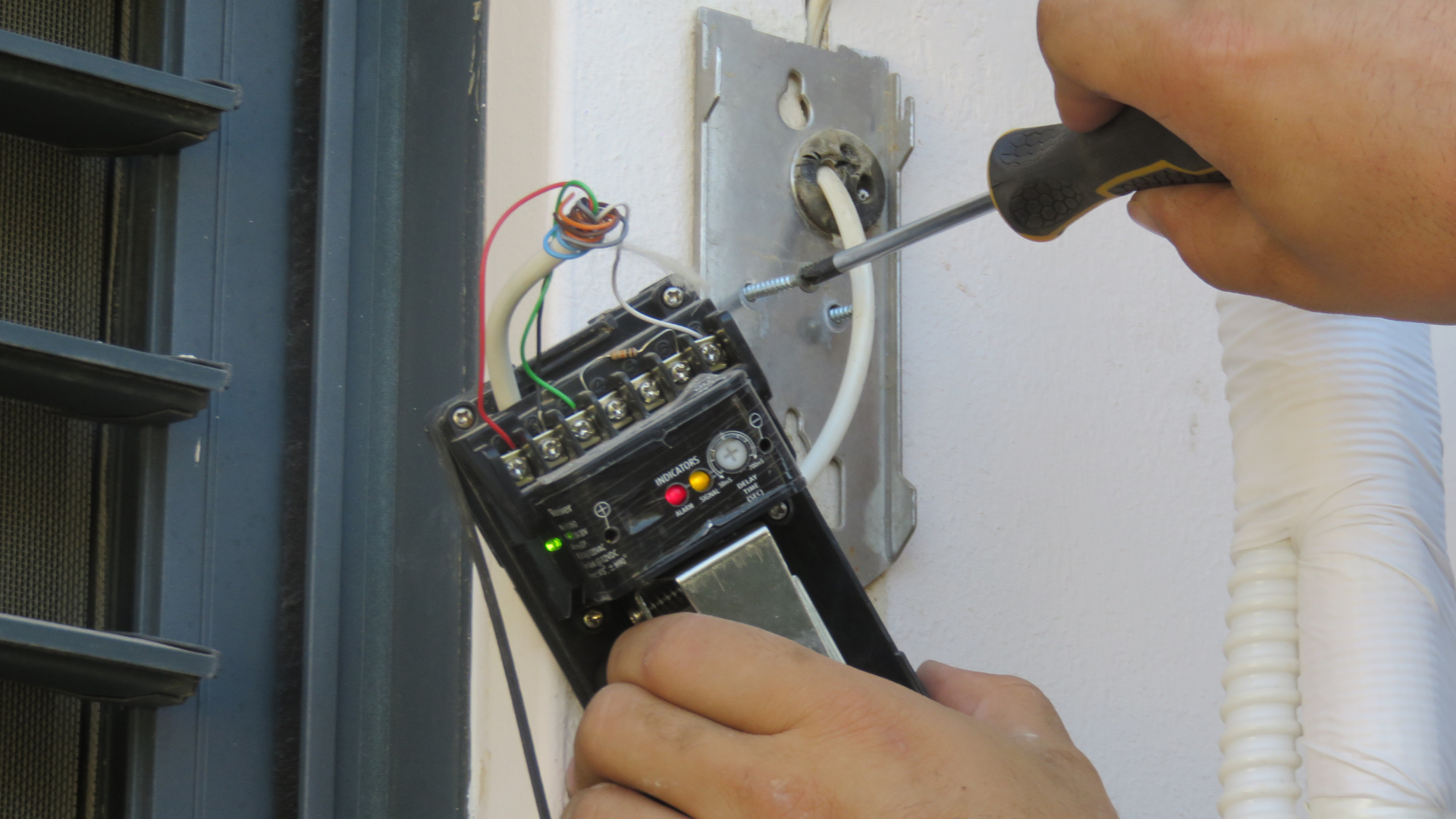 A person is using a screwdriver to fix a device on a wall.