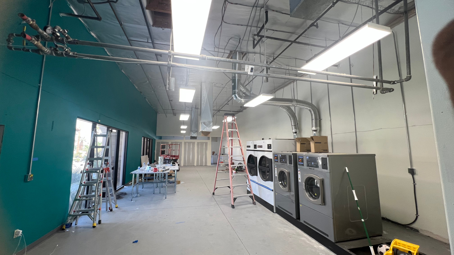 A laundromat with a row of washing machines and a ladder.