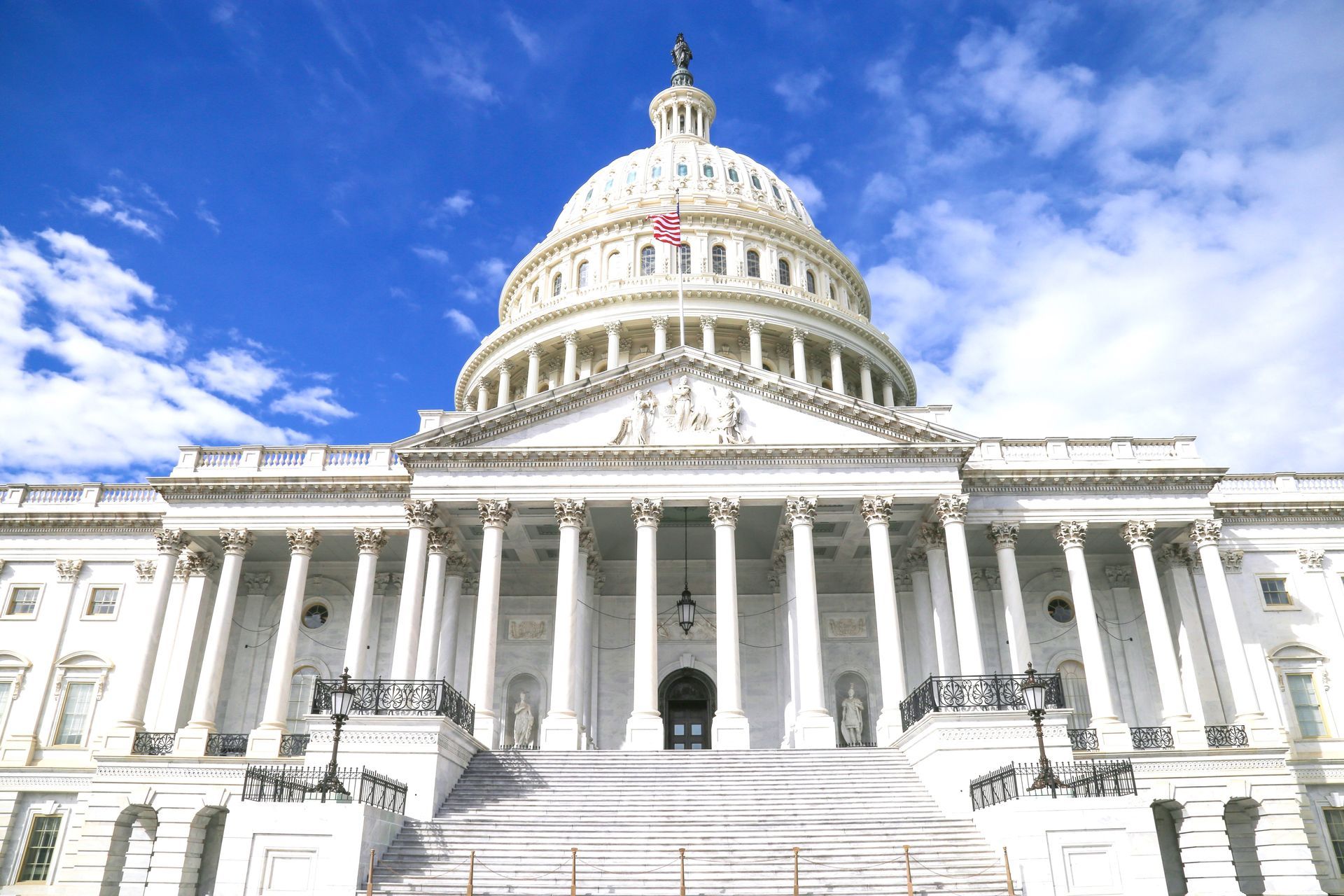United States Capitol Building, white with dome, on a green lawn under a blue sky with clouds.