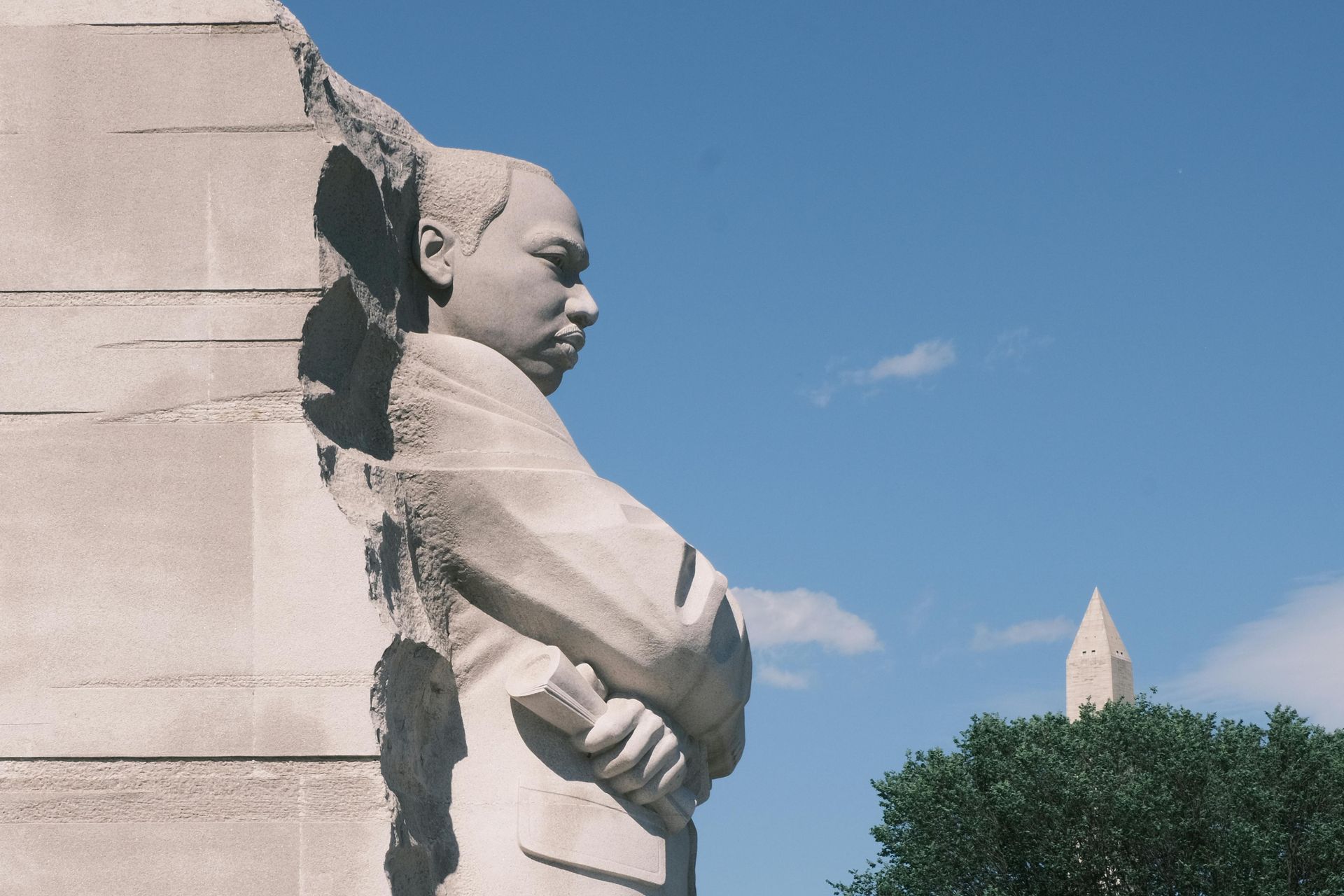 Statue of Martin Luther King Jr., Washington D.C., with the Washington Monument in the background, blue sky.