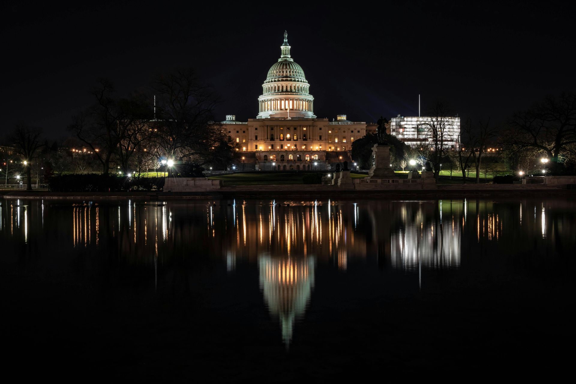 U.S. Capitol building at night, reflected in calm water; illuminated dome, lights.