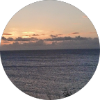 Sunset over calm ocean; orange and pink sky, gray water.