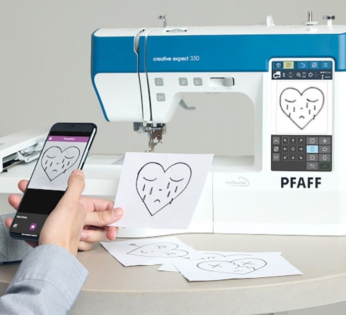 A person is holding a cell phone in front of a pfaff sewing machine