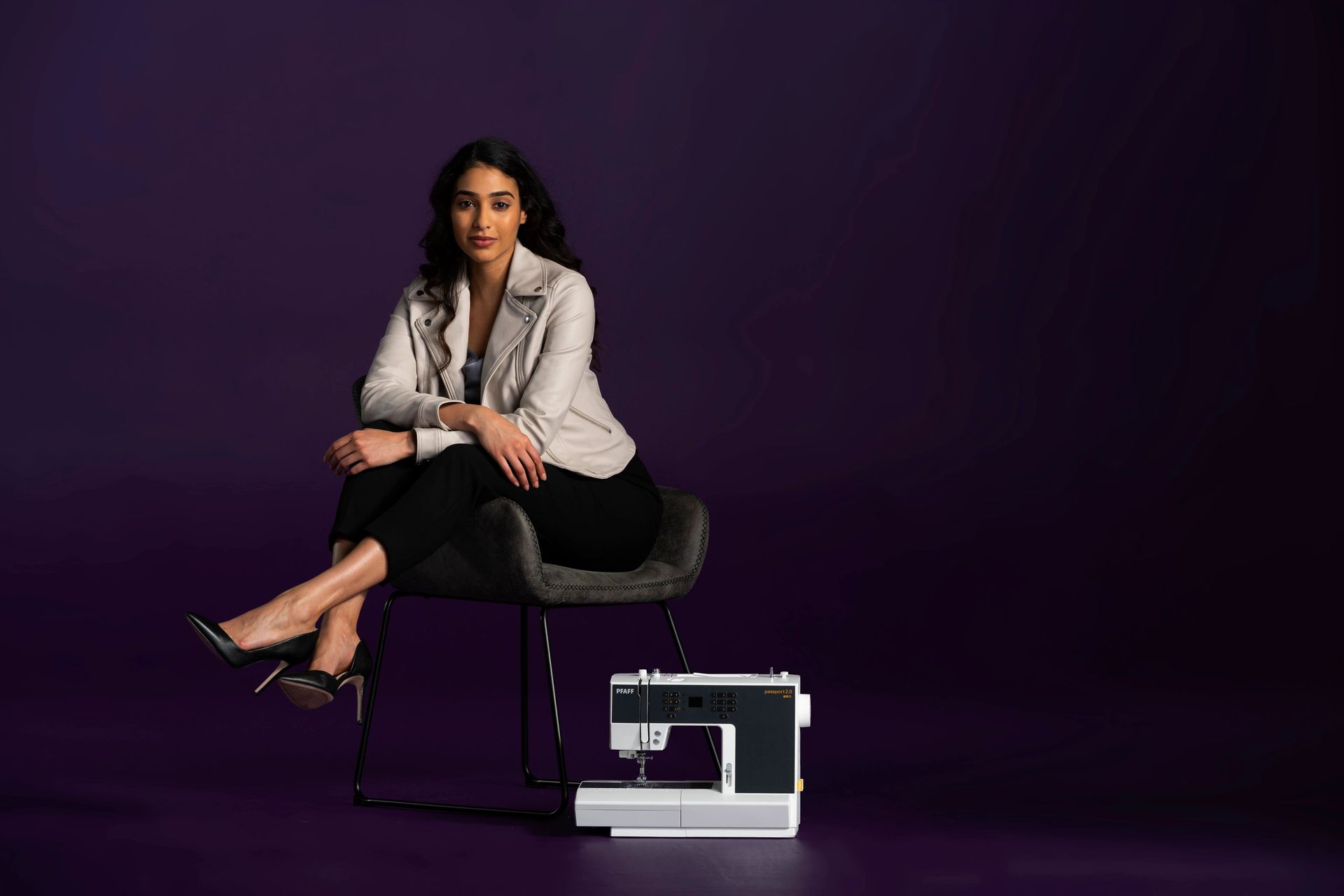 A woman is sitting on a chair next to a sewing machine.