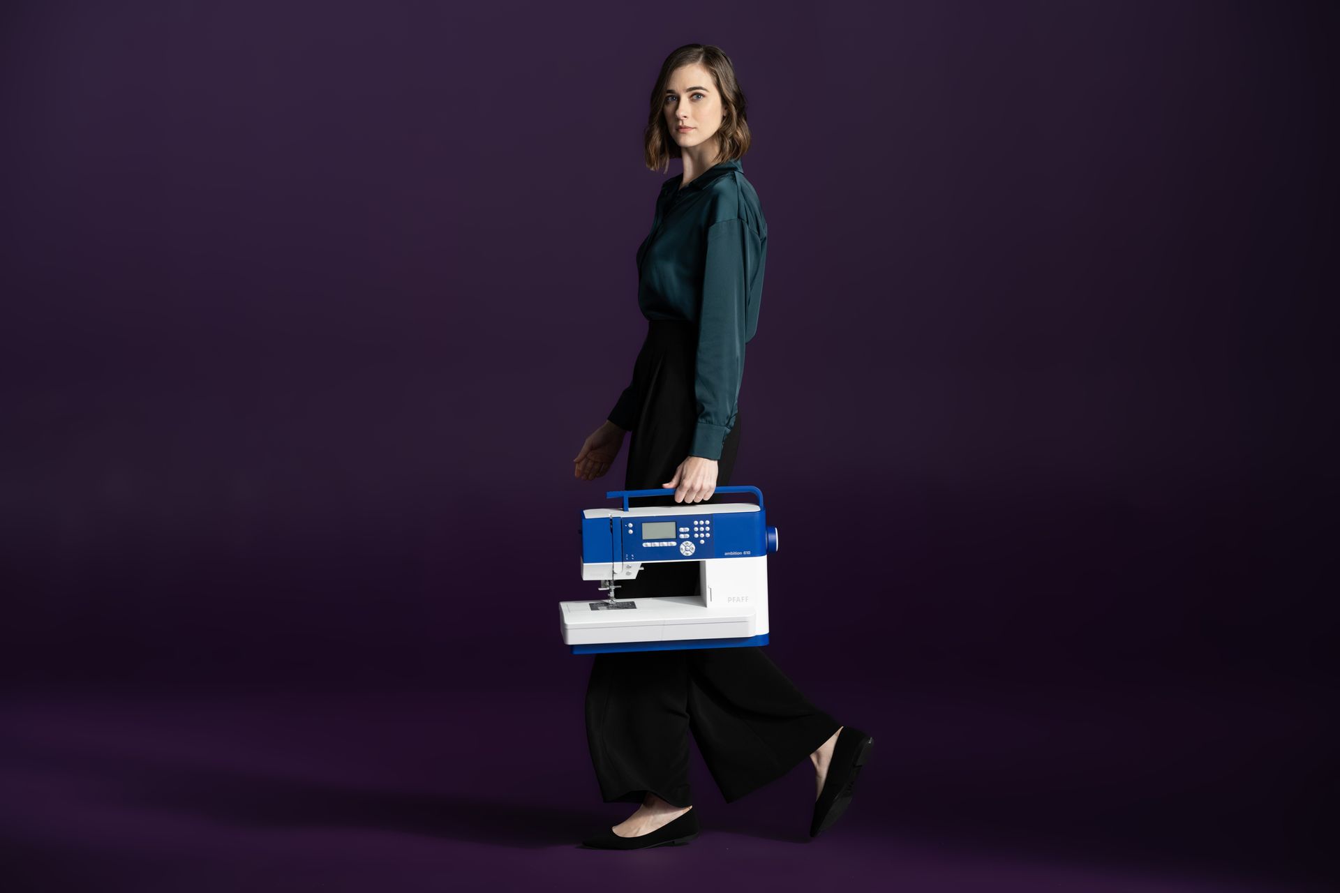 A woman is carrying a sewing machine on a purple background.