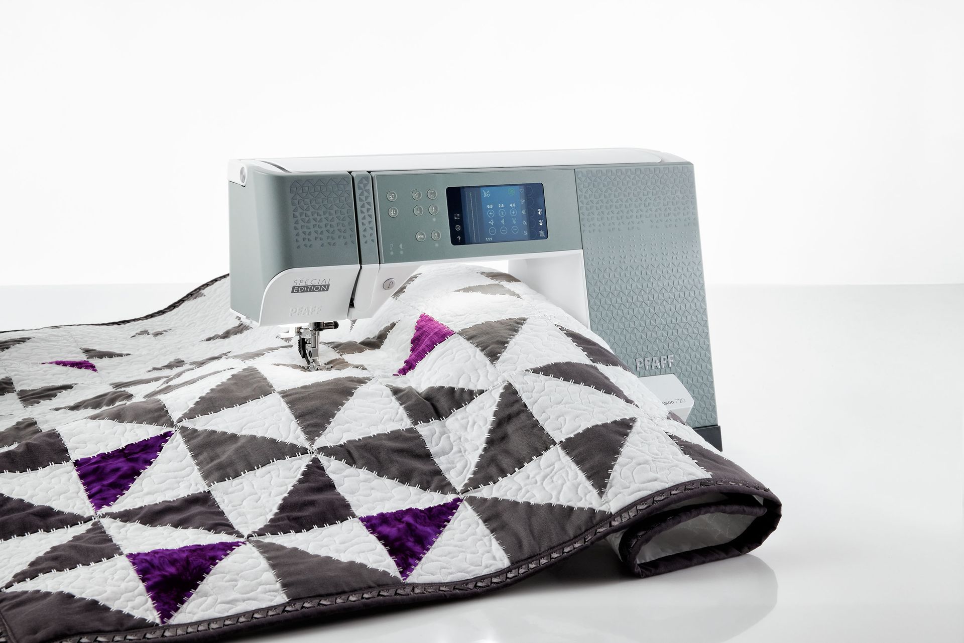 A sewing machine is sitting next to a quilt on a table.