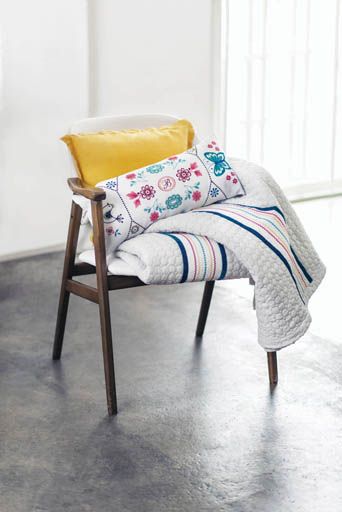 A chair with a blanket and pillows on it.