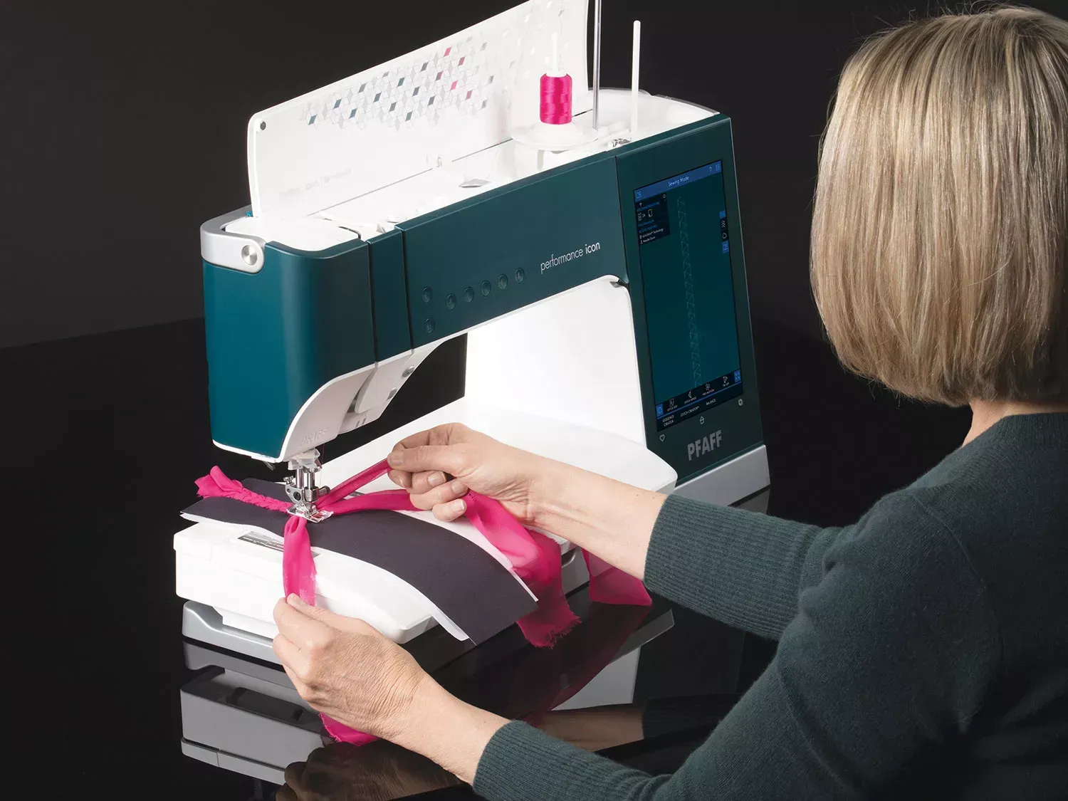A woman is using a sewing machine to sew a pink ribbon.