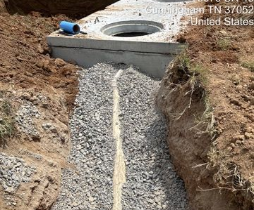 Gravel-filled trench leading to a concrete drainage structure in Cunningham, TN, with a blue pipe nearby.
