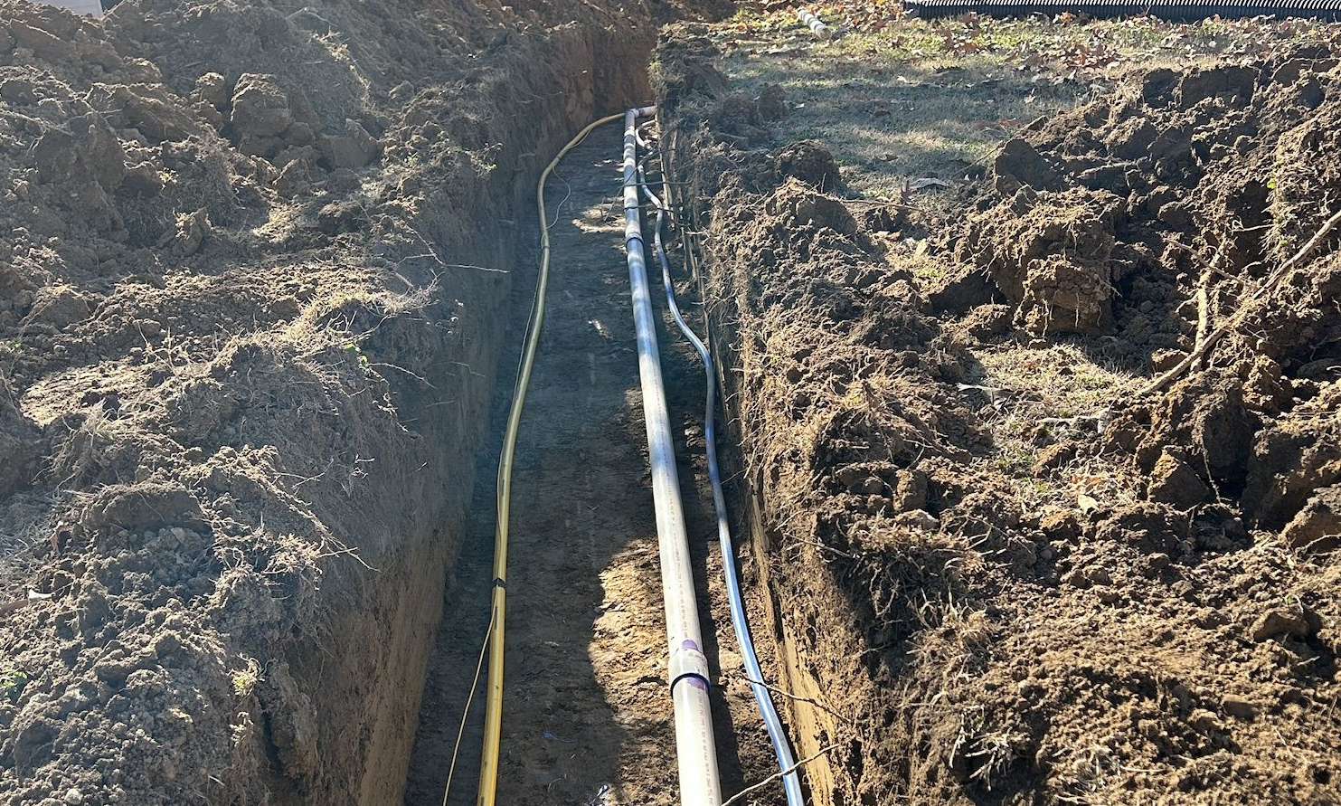 Man installing a green septic tank lid into concrete base, surrounded by soil and white pipes.