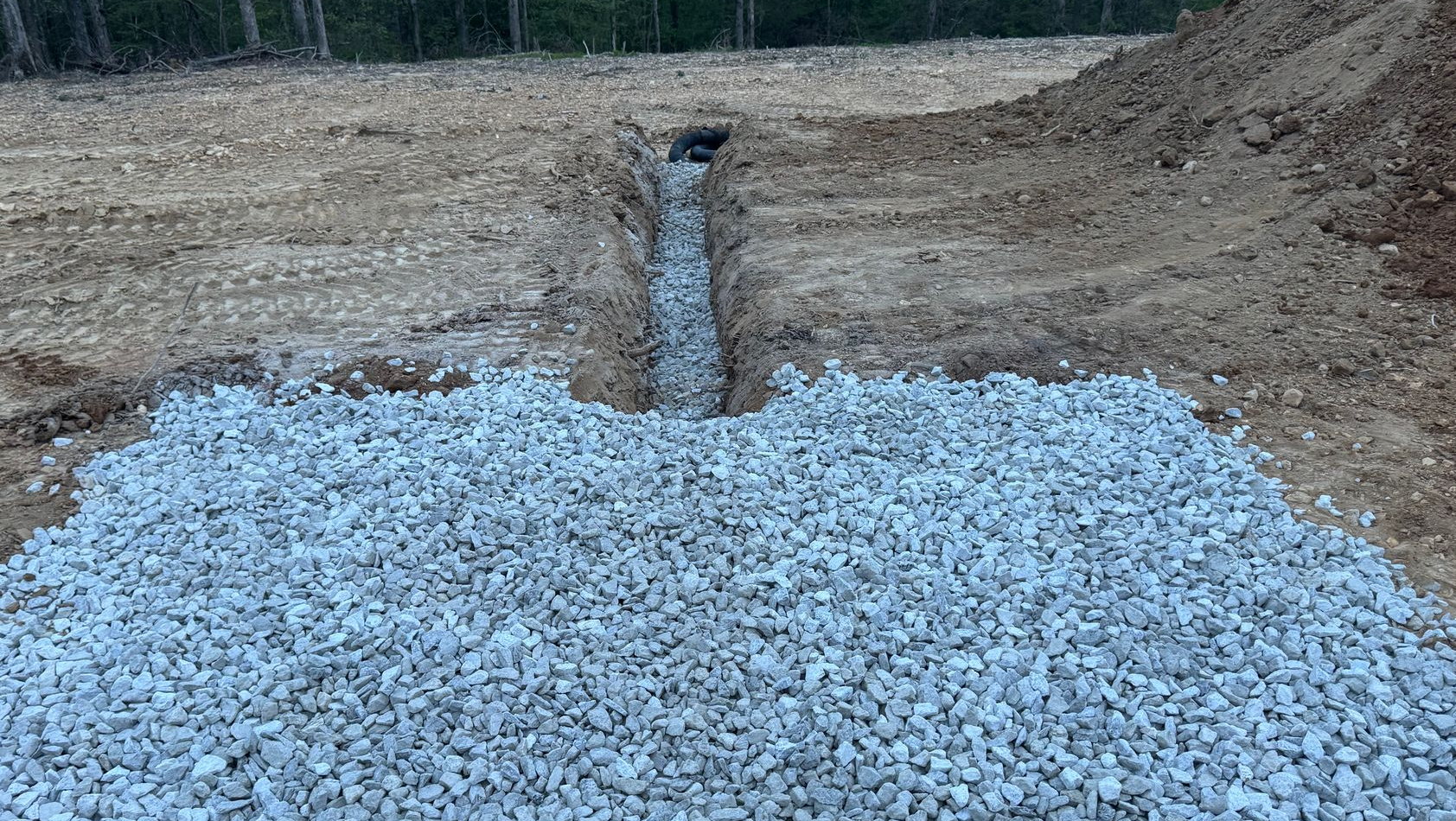 A drainage ditch filled with gravel in a cleared area.