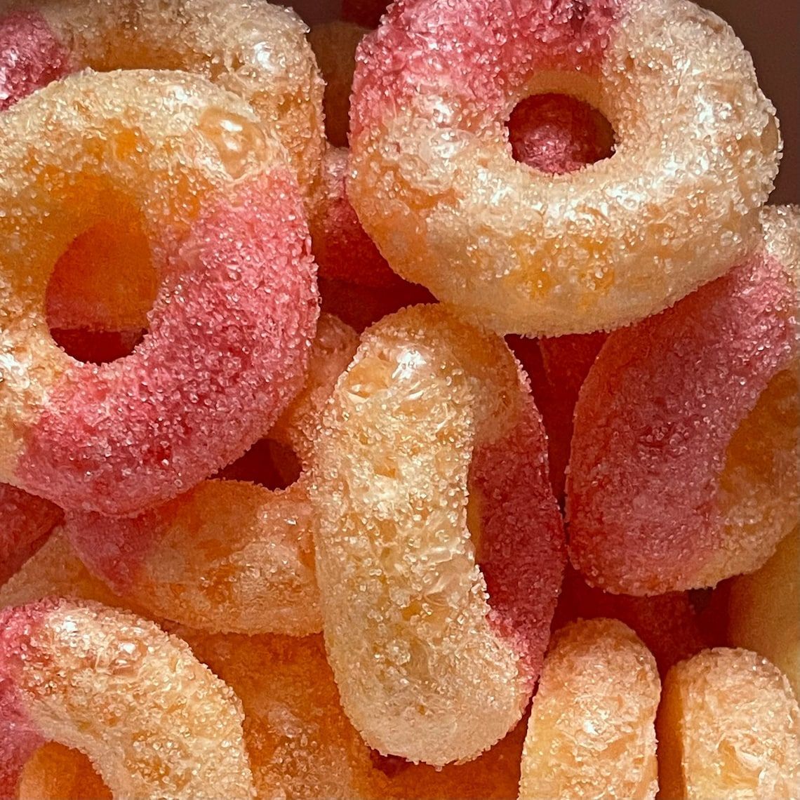 Close-up of peach-flavored gummy candies, with pink and yellow rings coated in sugar.