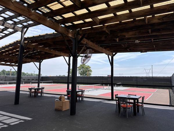 Outdoor dining area with tables under a shaded wooden structure, overlooking a rooftop space.