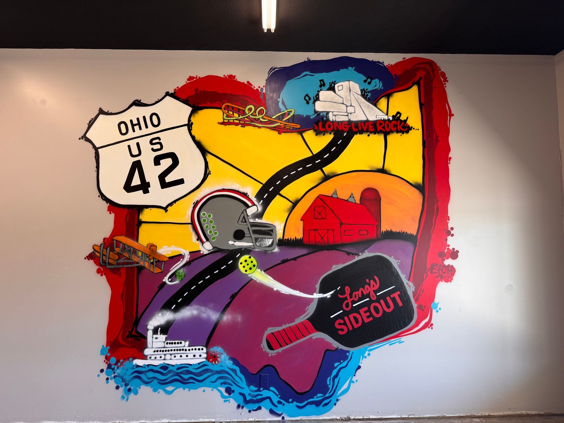 Mural of Ohio: US 42 sign, road, football helmet, paddle, and boat. Bright colors on a white wall.