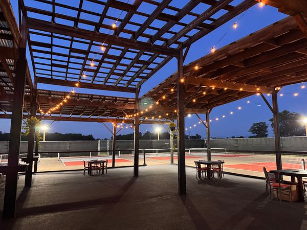 Outdoor patio with string lights, wooden pergola, tables, and chairs at dusk.