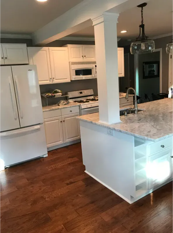 White kitchen with white cabinets, island, and appliances, brown hardwood floor.