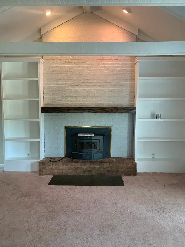 A fireplace with built-in white bookshelves. A brick wall is painted white above the fireplace.