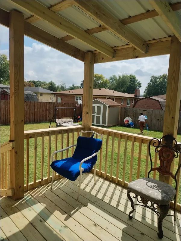 A porch with a blue chair, overlooking a backyard with a shed and people.