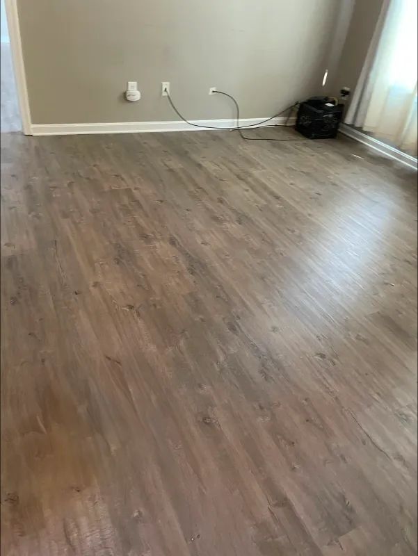 Light brown wood-look flooring in a room with neutral walls. A black trash can is in the corner.