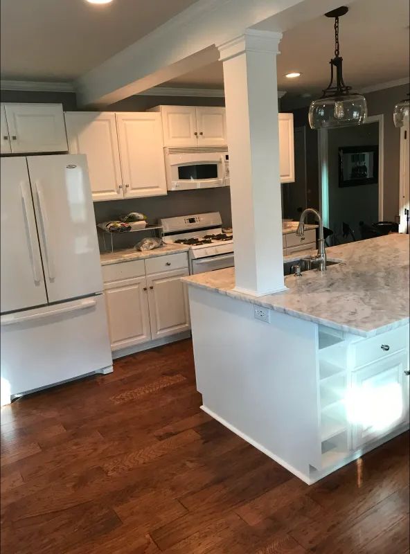 White kitchen with island, wood floor, white cabinets, stainless steel appliances, and overhead lighting.