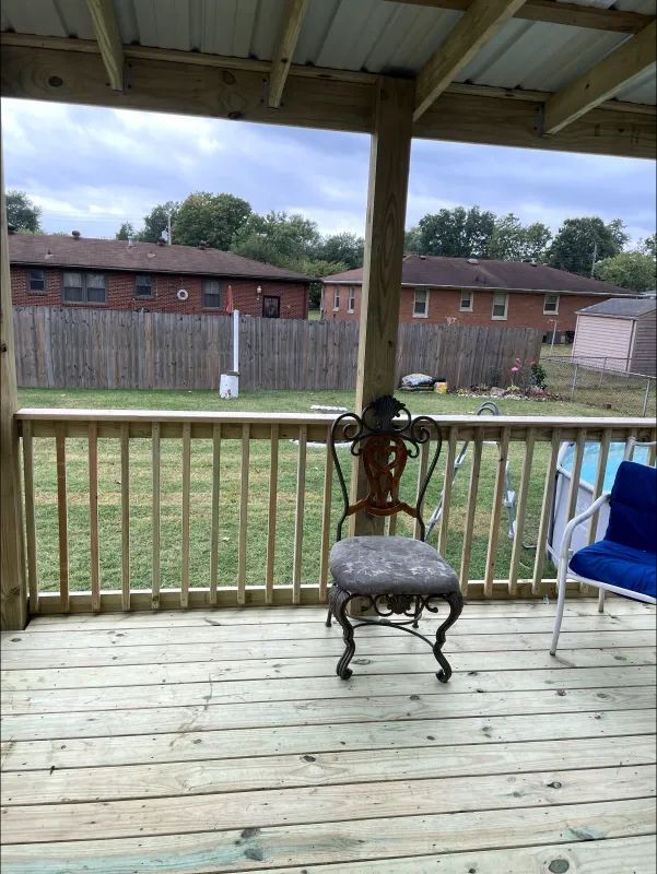 A porch with a decorative chair, overlooking a fenced backyard with neighboring buildings.