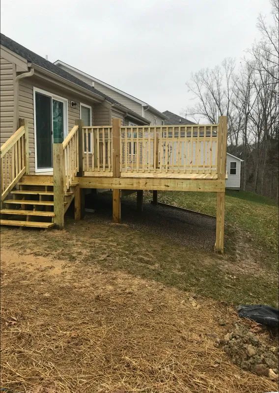 Wooden deck with stairs attached to a beige house on a grassy hill under an overcast sky.