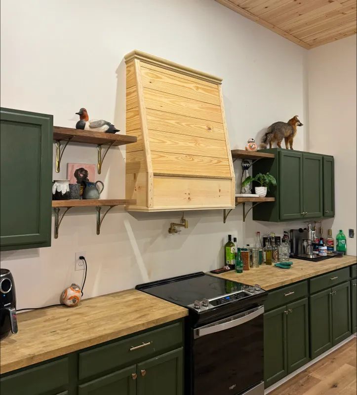 Green kitchen with wooden countertops, range, and unique wooden range hood.