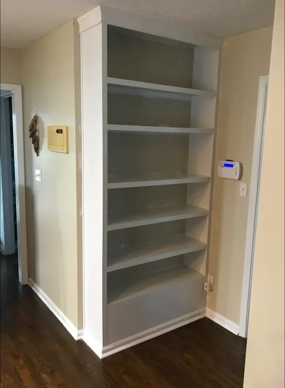 White built-in bookshelf in a corner of a room with cream walls and dark wood floor.