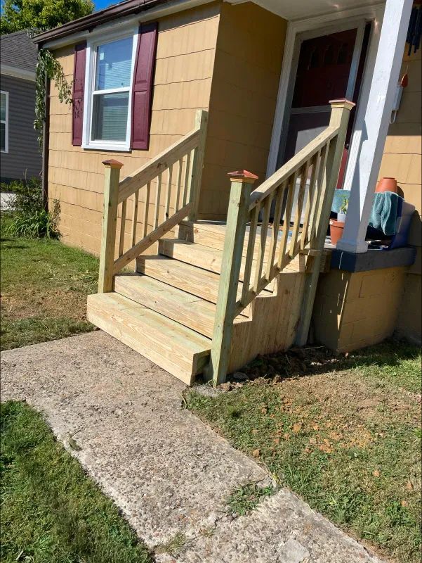 Wooden steps and handrails leading to a house door. Concrete path in front, green grass on the sides.