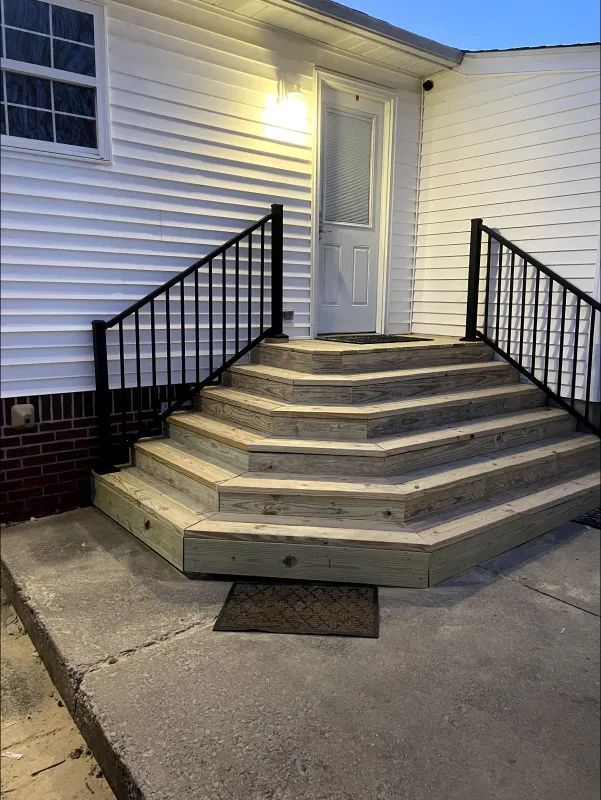 Outdoor stairs leading to a white door, with black handrails, gray concrete, and white siding.