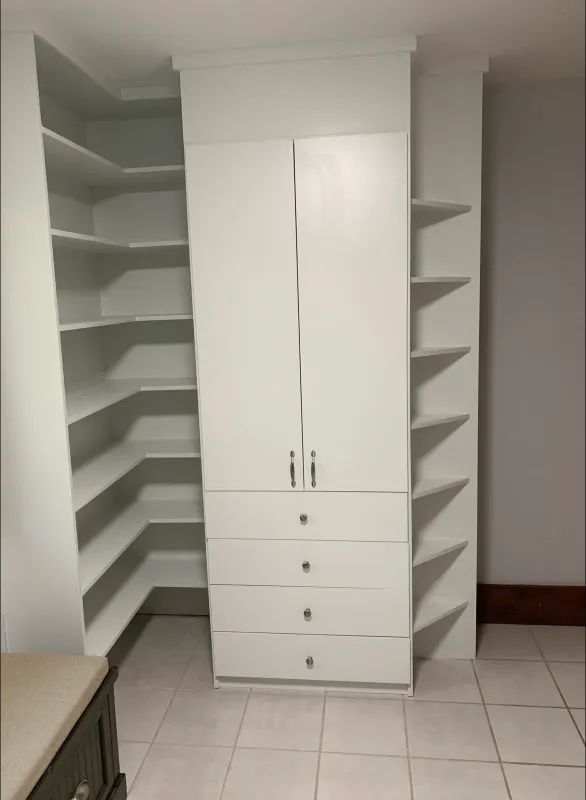 White built-in closet with corner shelving, drawers, and doors in a room with tiled floor.