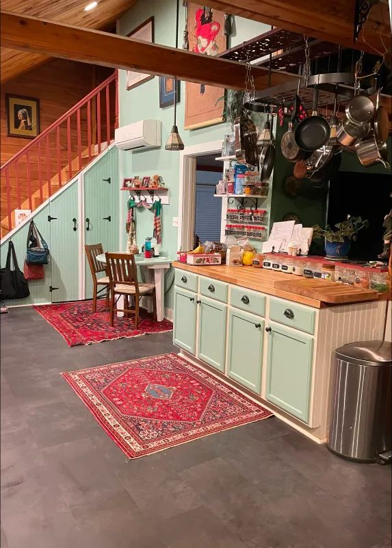 Kitchen with a red rug, light green cabinets, and wooden stairs.