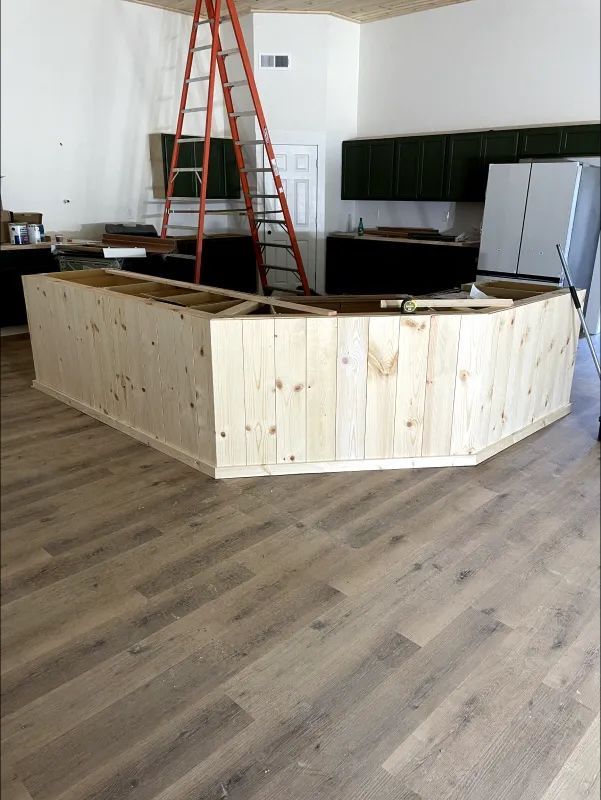 A wooden bar under construction in a room with hardwood floors. An orange ladder leans against the wall.