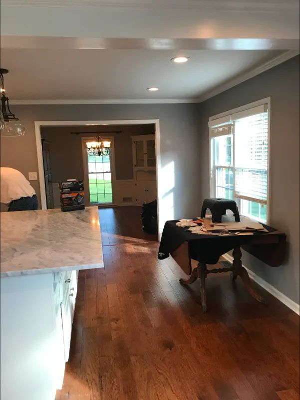 Wooden floors, gray walls, and a white kitchen island in a kitchen with a small table by the window.