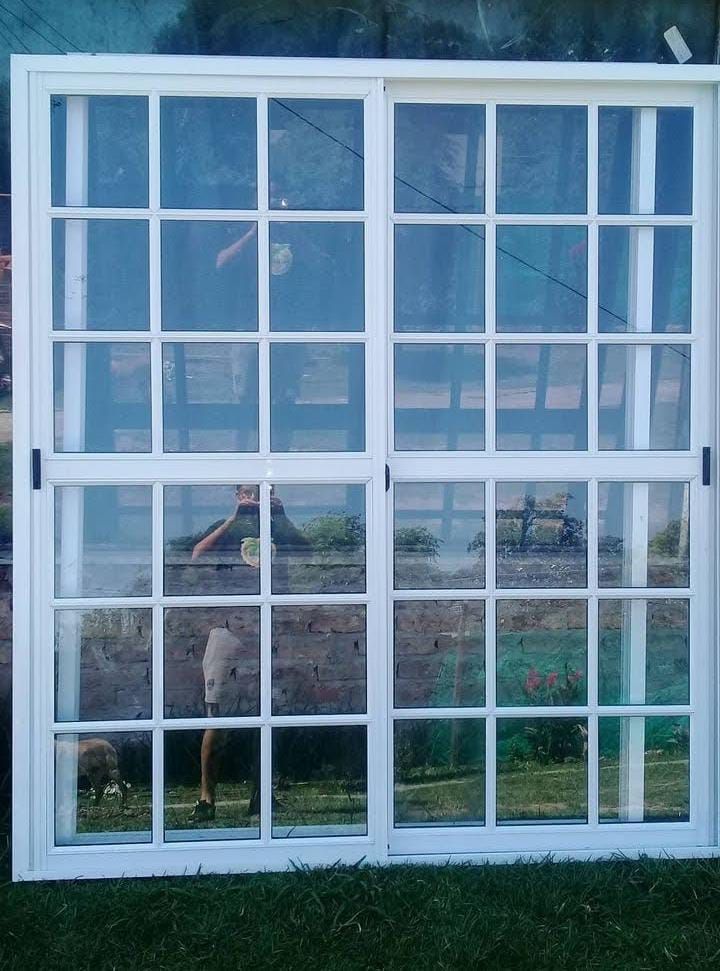 Ventana corrediza con marco blanco y múltiples paneles, que refleja una escena al aire libre con césped y una persona.