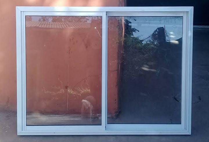 Ventana corrediza con marco blanco contra una pared de color marrón rojizo y árboles visibles a través del vidrio.