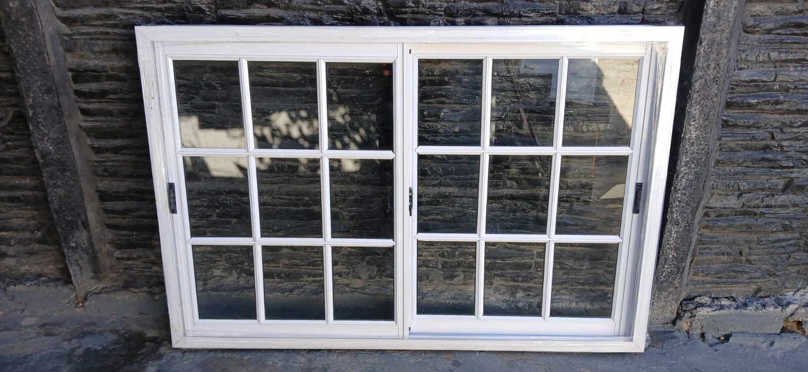 Ventana con marco blanco y múltiples paneles contra una pared de ladrillos desgastados.