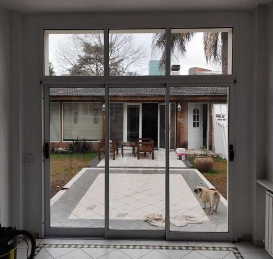 Las puertas corredizas de vidrio se abren a un patio trasero con un perro y una mesa.